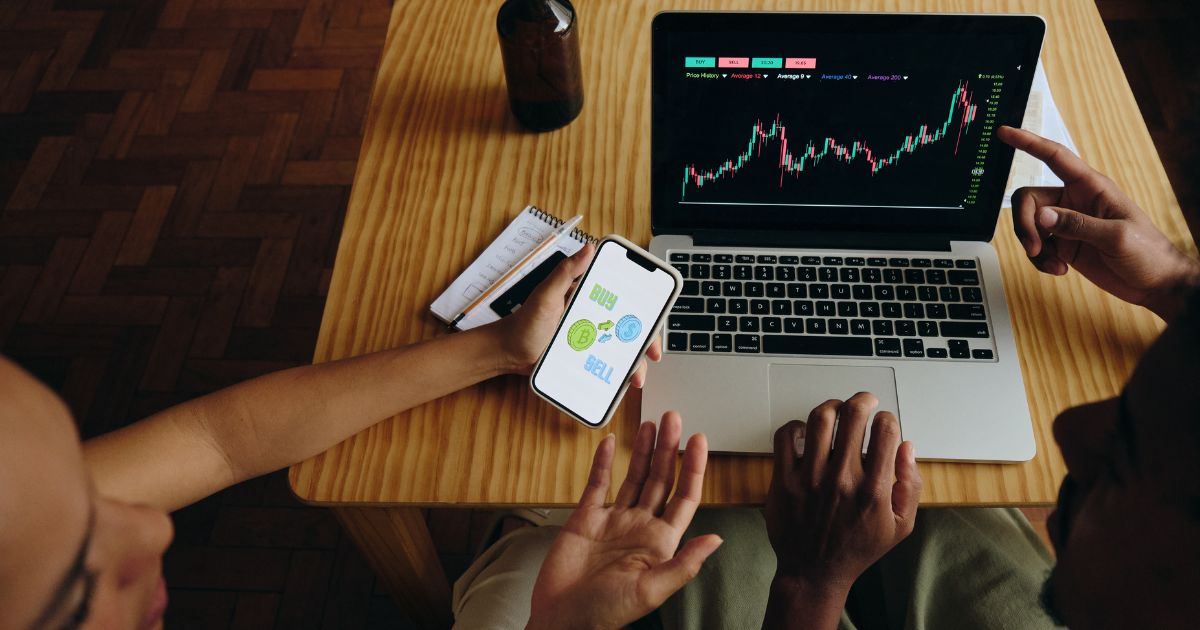 Computer with stocks and man holding phone with but and sell image